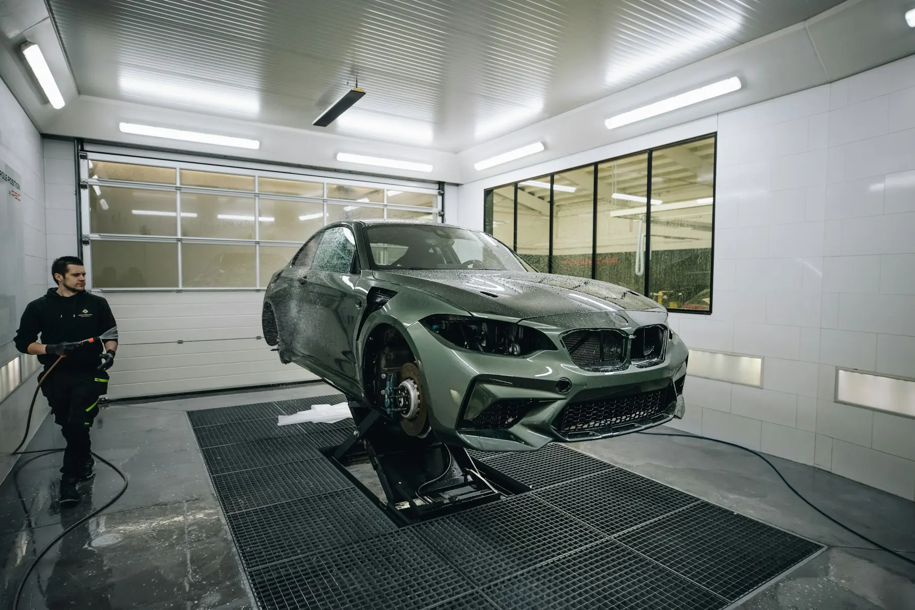 A car on a booth ramp with its wheels off, being washed down before repair