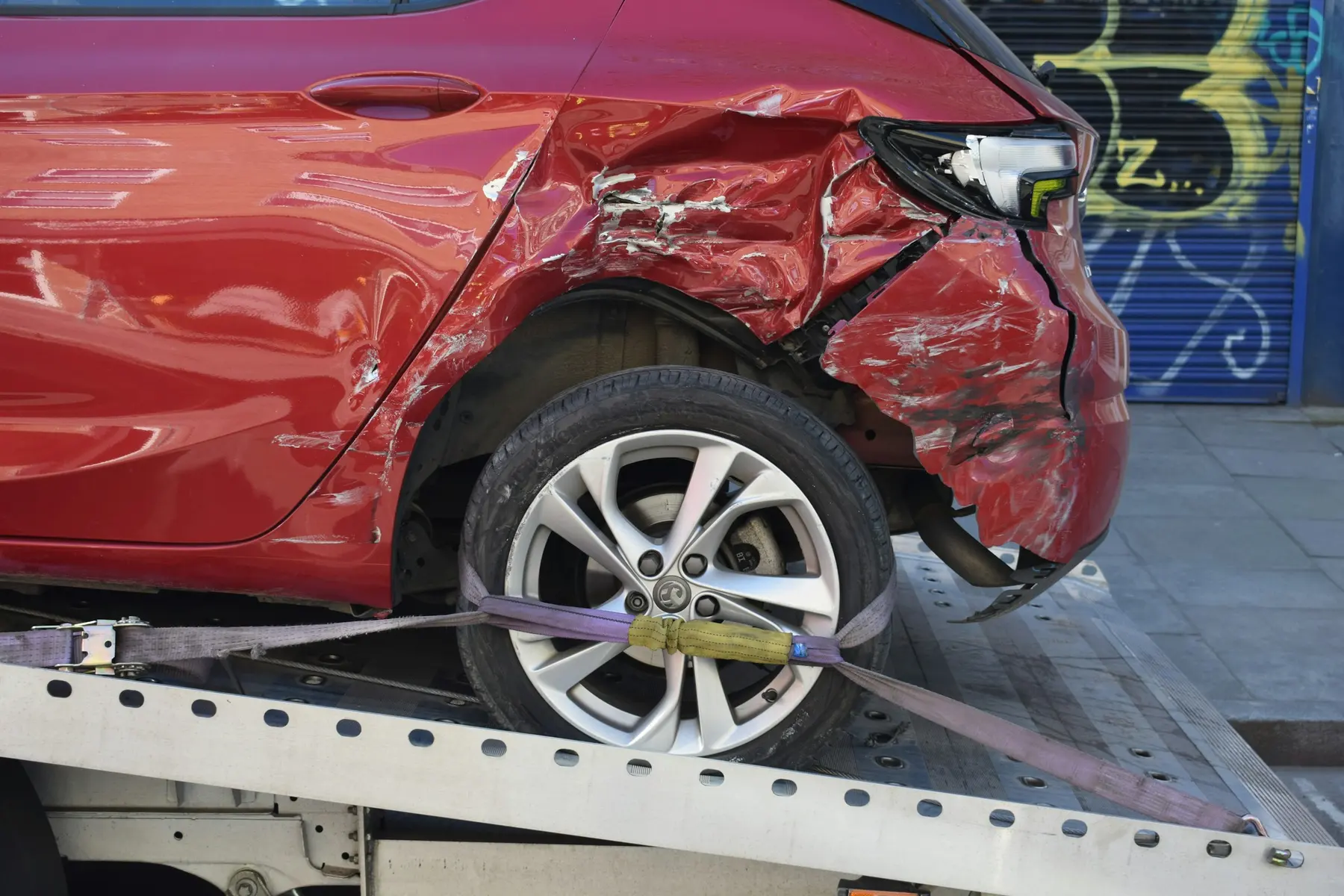 A damaged red car strapped to a flatbed tow truck