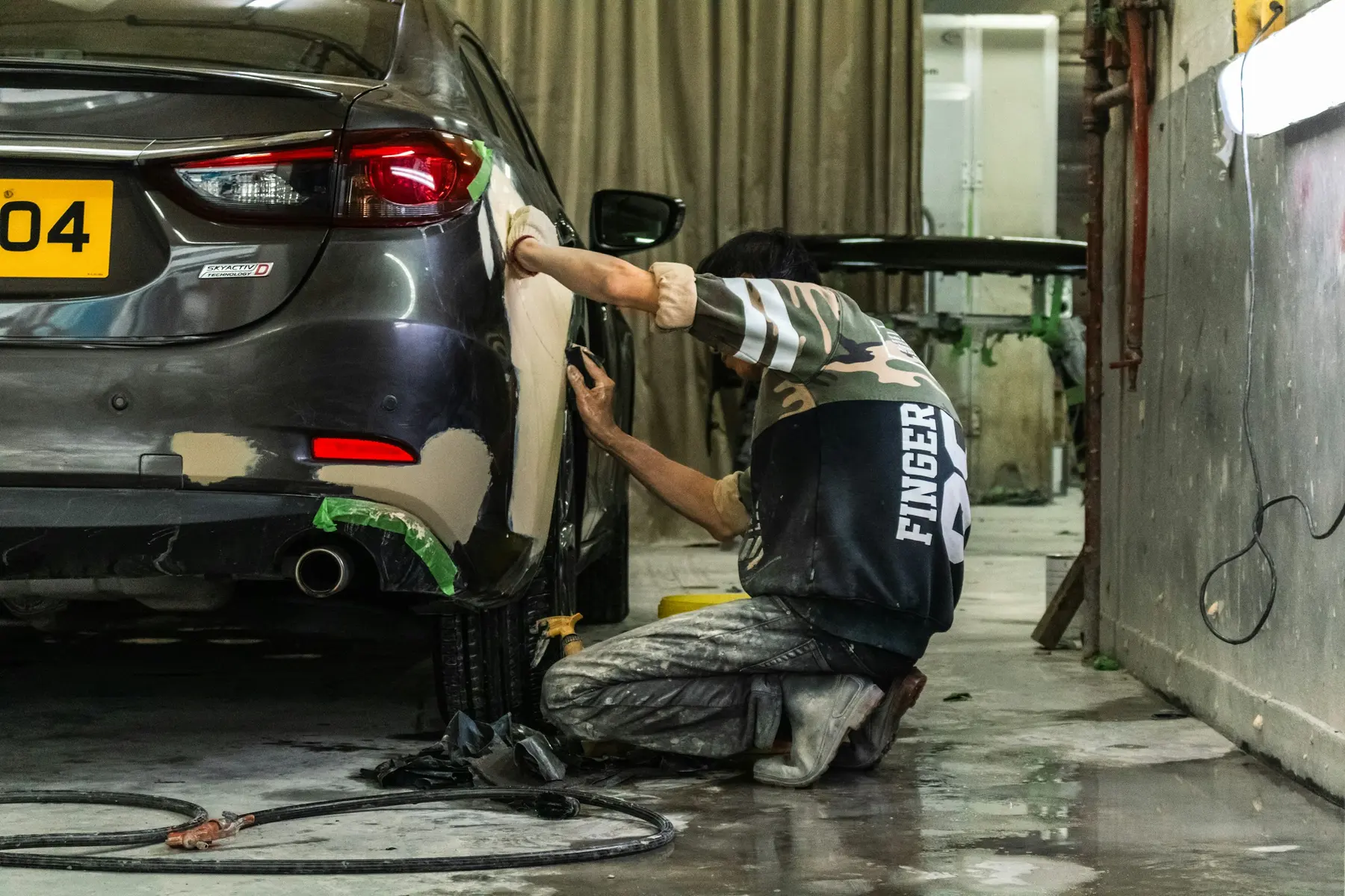 A panel beater sanding the rear quarter of a car in a workshop